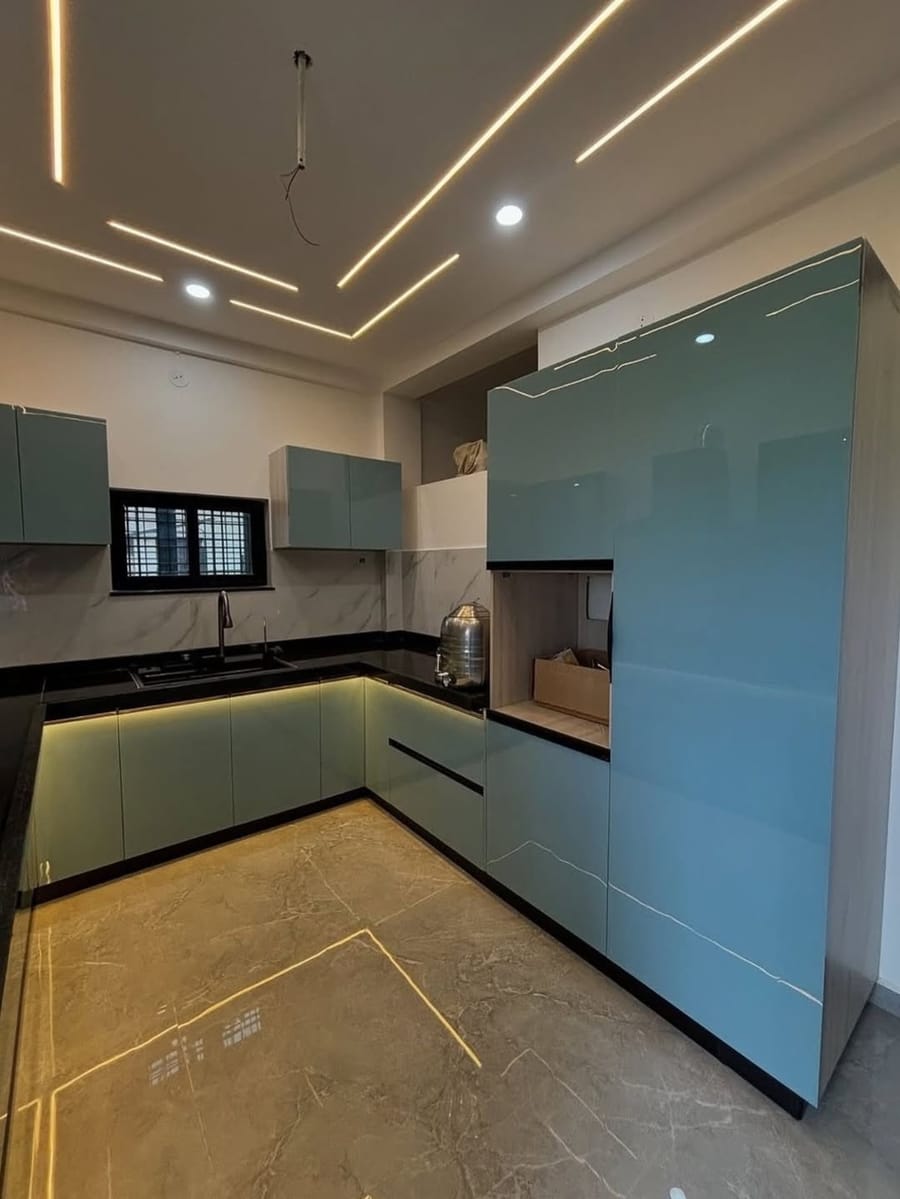 L-shaped modular kitchen with sea-green glossy cabinets and cove lighting, by Trimurti Interiors